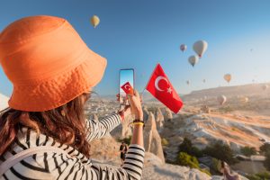 a travel blogger girl takes photos of flying balloons in Cappadocia and the Turkish flag. Social media influencer